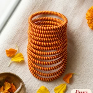 Red and yellow striped thread bangles stacked on cream handloom with marigold petals and a brass bowl