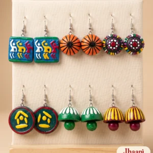 Six pairs of terracotta earrings on a cream display card: blue dancing-figure tiles, orange domes, dotted domes, green discs, green and maroon jhumkas