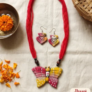 Red and yellow terracotta butterfly necklace on red cotton threads laid flat on cream handloom with matching earrings, marigold petals and a brass bowl