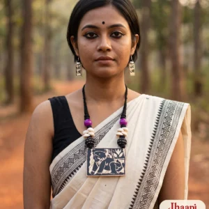 Woman in an off-white black-bordered saree on a red-earth path among sal trees, wearing the Jhaapi hand-painted wooden necklace and Bengali alphabet earrings